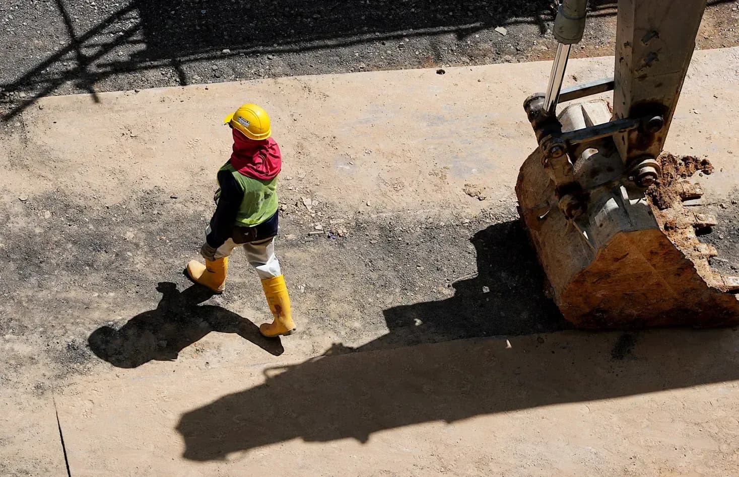 tiefbau glasfaser – Bauarbeiter mit Schutzkleidung neben Baggerlöffel auf Baustelle