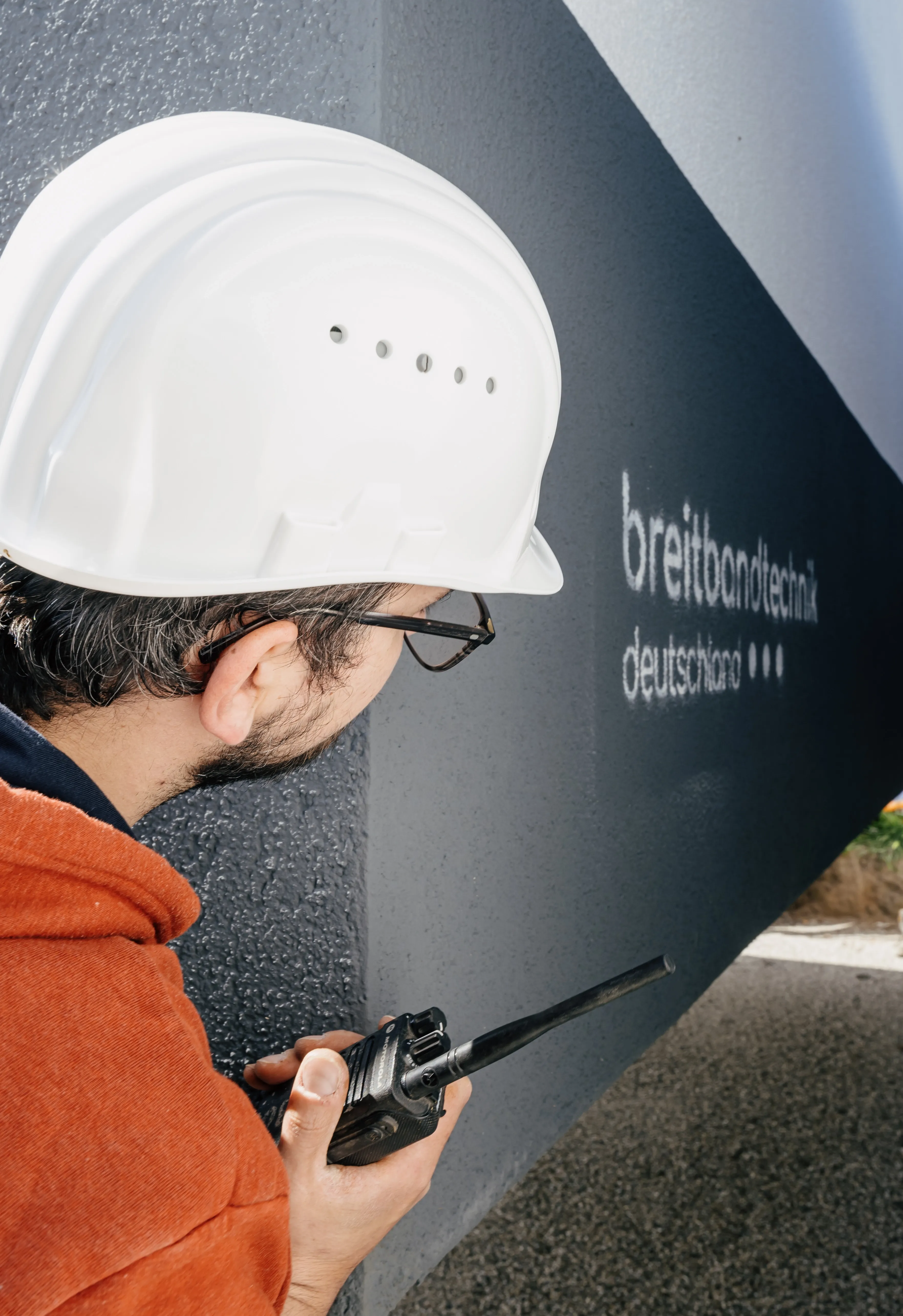 Mitarbeiter mit Schutzhelm und Funkgerät vor Gebäude der Breitbandtechnik Deutschland GmbH